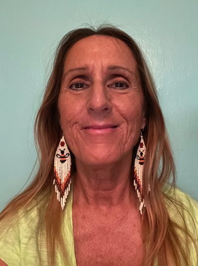 Woman with long earrings smiling against a teal background.