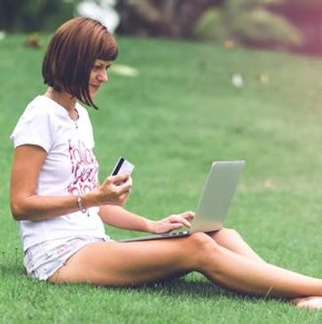 Person sitting in lawn with laptop and credit card.