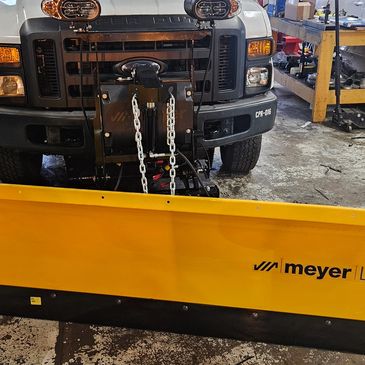 Yellow Meyer snowplow attached to front of white truck.