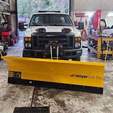 White truck with yellow Meyer Lot Pro snow plow attachment.