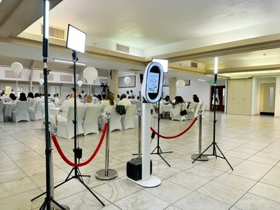 Indoor event with guests dressed in white, photo booth setup with lights.