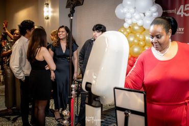 People at an indoor event with a photobooth and balloon decoration.