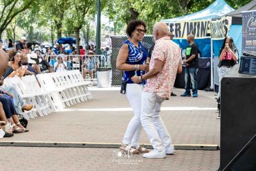 A joyful couple dancing at an outdoor event with a seated audience.