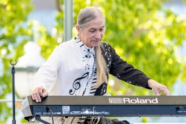 Elderly man playing a Roland keyboard outdoors.
