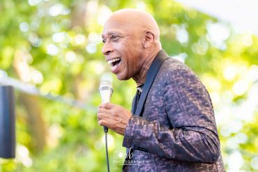Smiling man singing into a microphone outdoors.