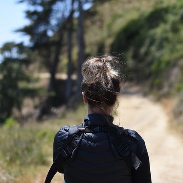 Woman hiking on a sunny trail surrounded by greenery.