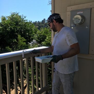 Man painting a balcony railing white on a sunny day.