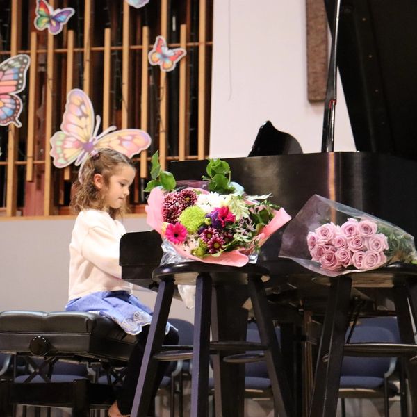 Young girl playing piano with flowers on top.
