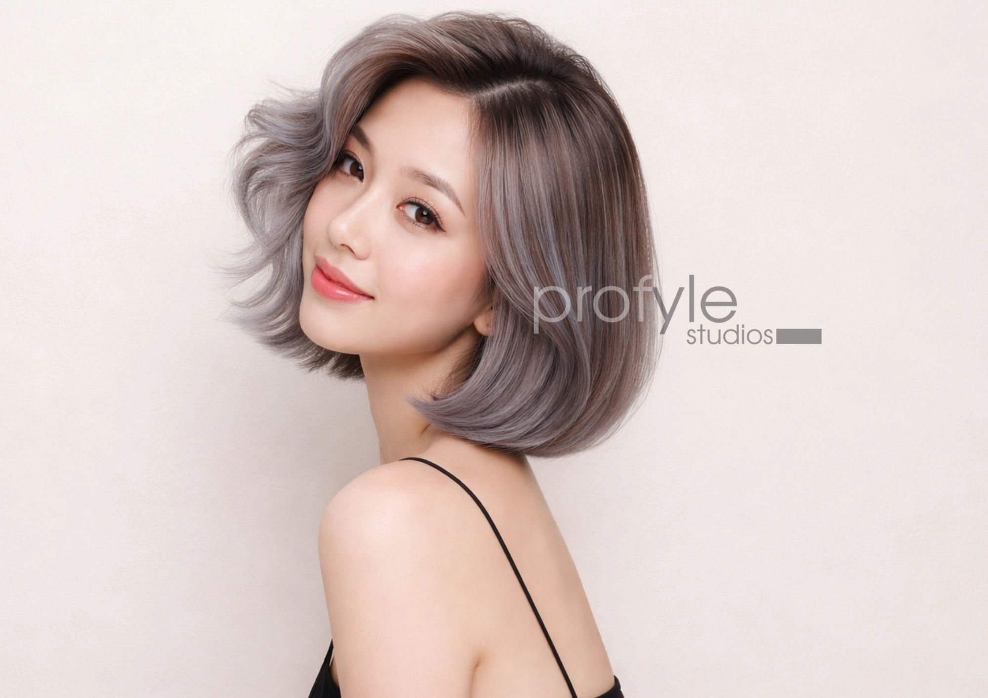 Smiling woman with stylish silver-gray bob haircut and soft makeup.