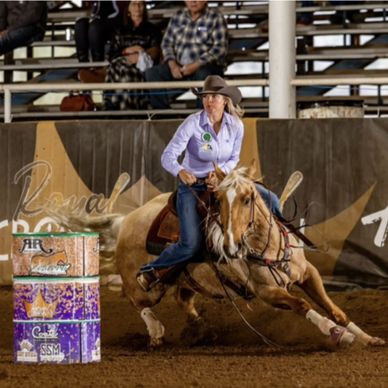 Woman in cowboy hat barrel racing on a horse at a rodeo arena.