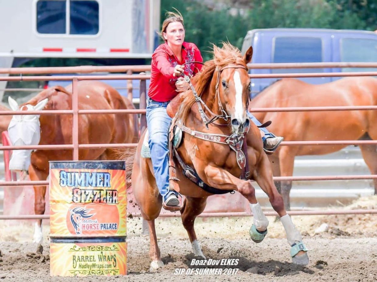 Woman riding a horse in a barrel racing event.