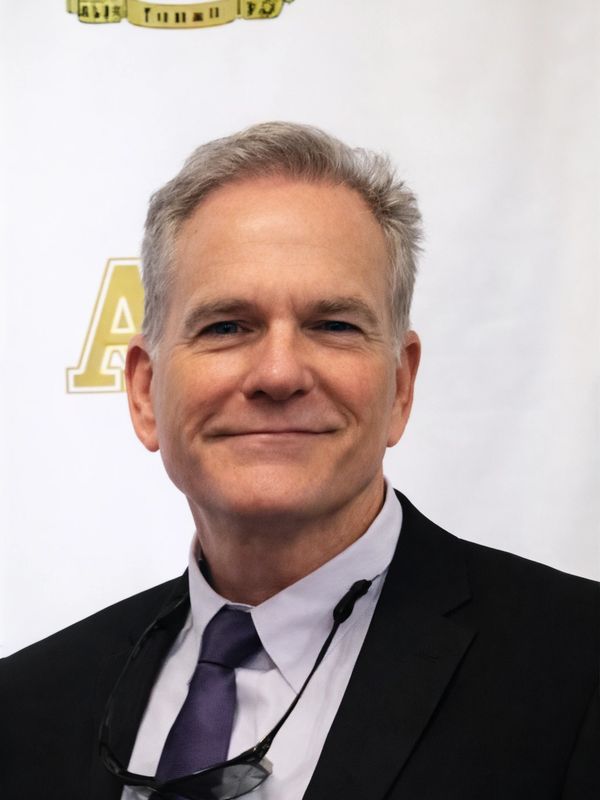 Middle-aged man in a suit and purple tie smiling at the camera.