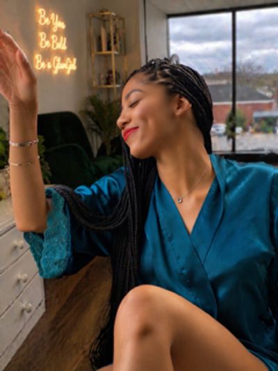 A woman in a blue robe smiles joyfully by a window.