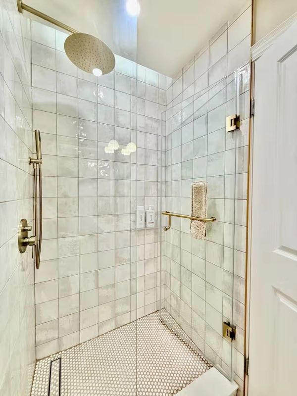 Modern glass shower with brass fixtures and tiled walls.