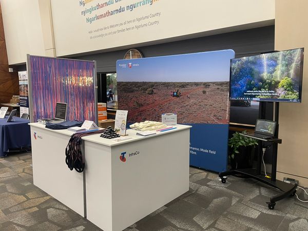 Exhibition booth showcasing Telstra InfraCo with informational displays and a video screen.