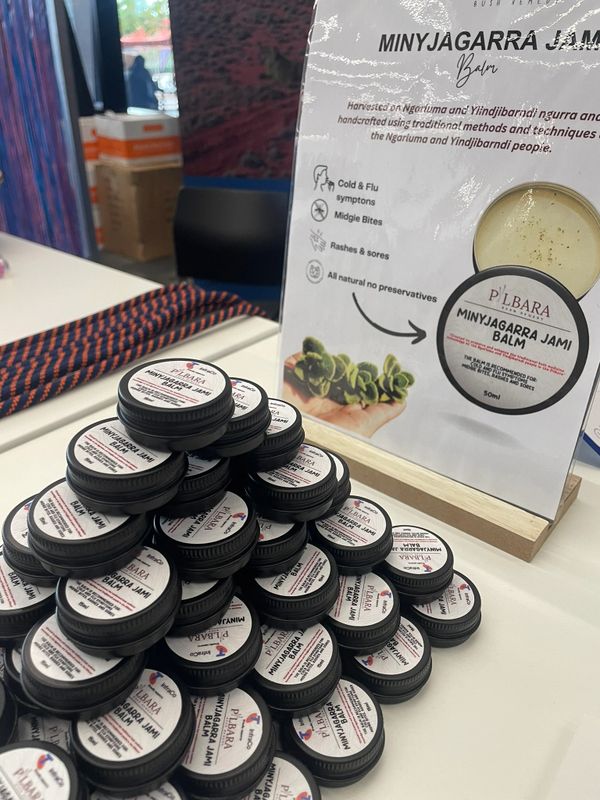 Stack of Minyjagarra Jami Balm containers on a table with an informational sign.