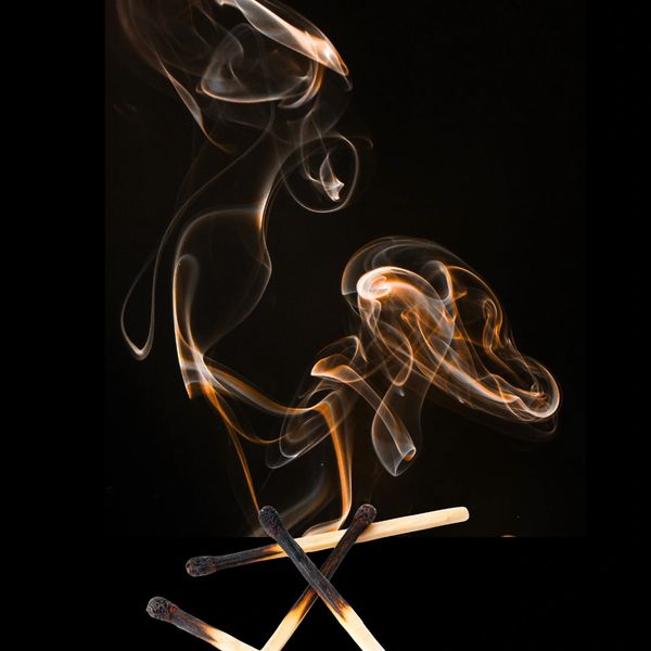 Burnt matches emitting swirling smoke against a black background.
