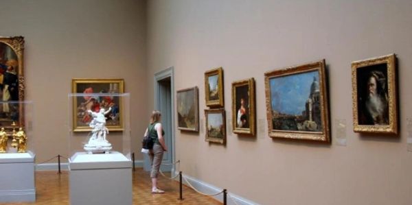 Visitor observing framed paintings in an art gallery.