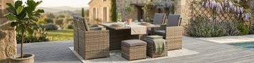 Outdoor wicker dining set on a wooden deck with cushions and a potted plant.
