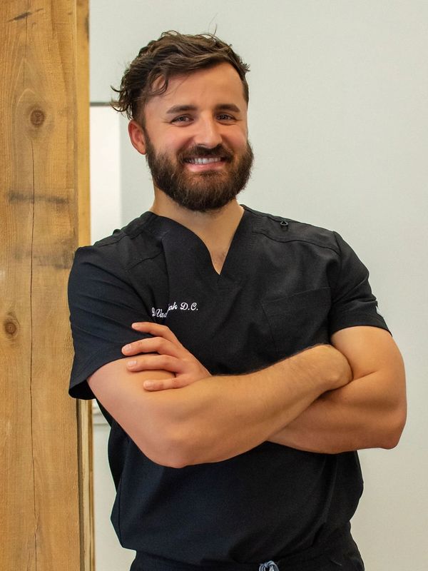 Smiling man in black medical scrubs with arms crossed.
