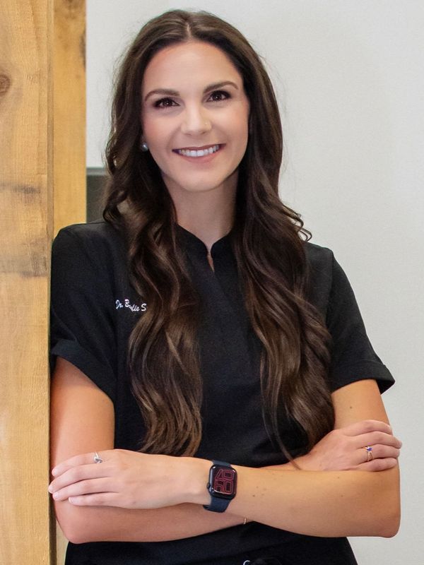 Smiling woman with long brown hair wearing black attire and a smartwatch.