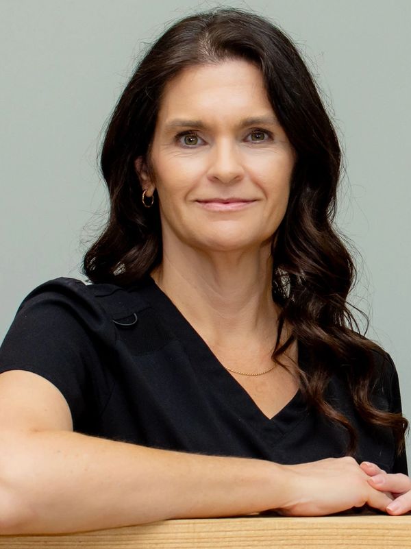 Confident woman with dark hair and black top smiling gently.