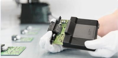 A person wearing white gloves holds a circuit board with a black heatsink.