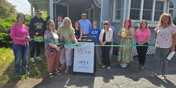 Group of people at a ribbon-cutting ceremony outside a house.