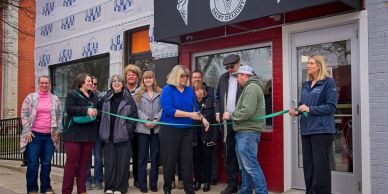 Group of people cutting a green ribbon at a storefront opening ceremony.
