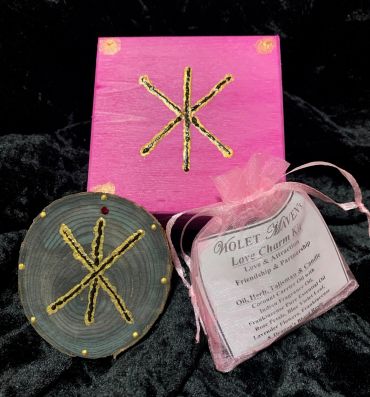 Mystical love charm kit with a wooden symbol and pink box.