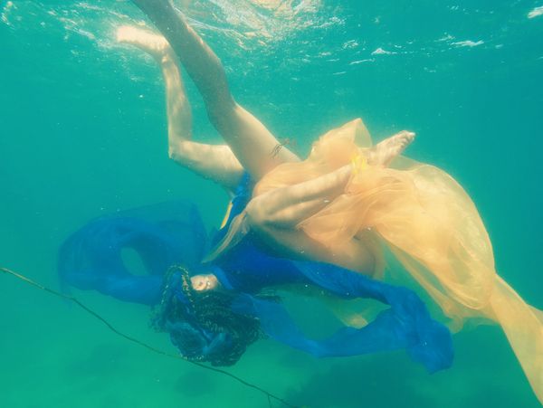 Two figures in flowing blue and yellow fabrics gracefully float underwater.