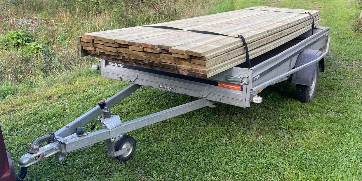 Metal trailer loaded with wooden planks on grassy ground.