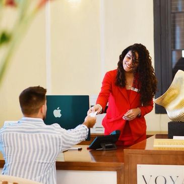 Hotel receptionist in red handing a card to a guest at the front desk.