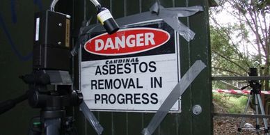 Danger sign for asbestos removal taped to a dark green door with cameras nearby.