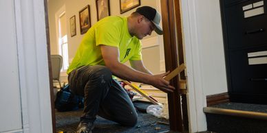 A worker in a neon yellow shirt repairing a door frame indoors.