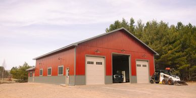 A large red metal garage with three doors and vehicles inside and outside.