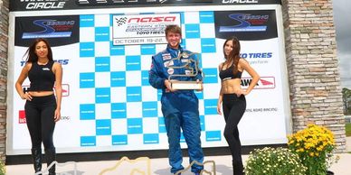 Race winner holding trophy on podium with two women.