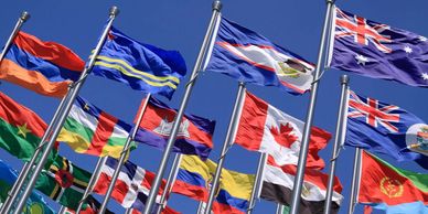 A group of international flags flying against a clear blue sky.