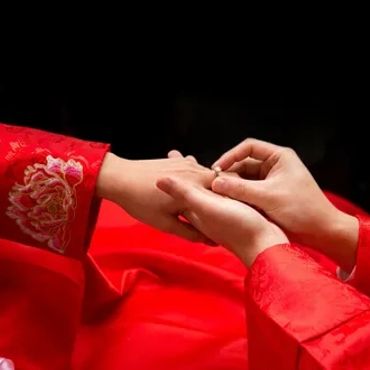 Hands exchanging a ring, dressed in traditional red attire.