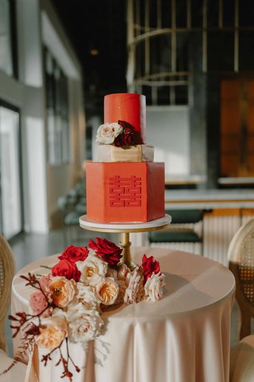 Elegant three-tier red wedding cake with floral decorations on a round table.