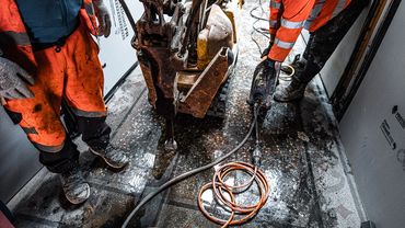 Construction workers using machinery to break concrete indoors.