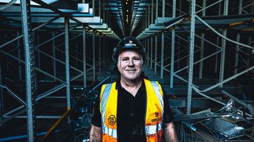 Warehouse worker in safety gear standing confidently amid metal racks.