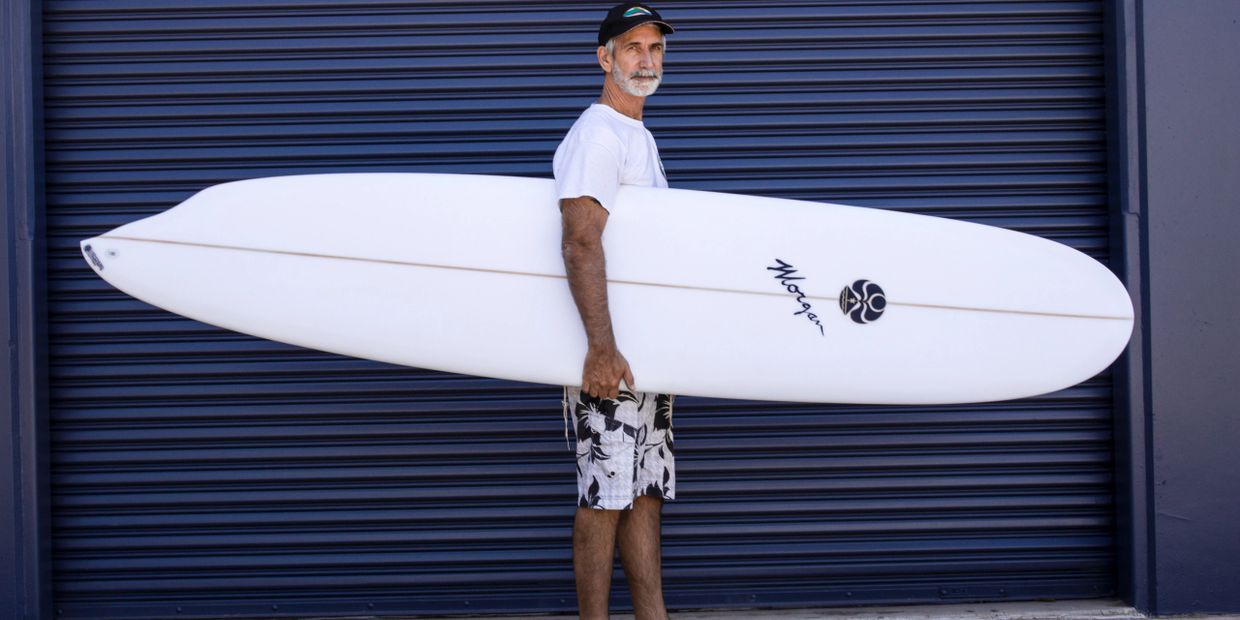 Man in casual wear holding a white surfboard against a blue shutter.