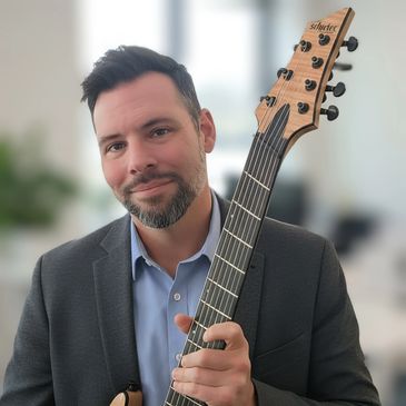 Man in a suit holding an electric guitar and smiling.