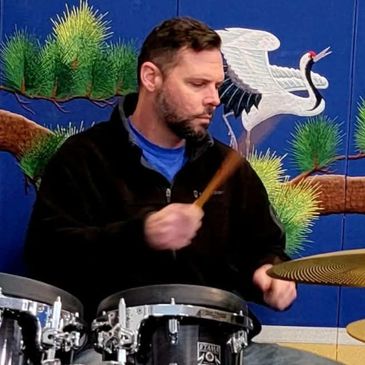 Man focused playing drums with colorful mural background.