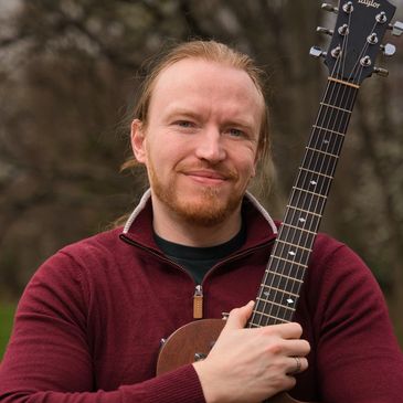 Man in a red sweater holding a guitar outdoors.