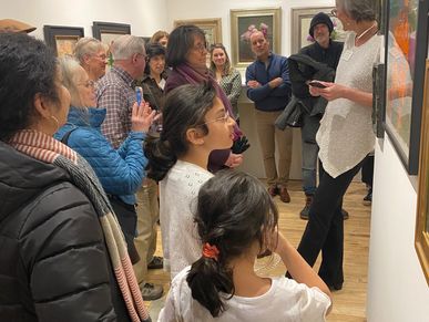 A group attentively listens to a guide in an art gallery.