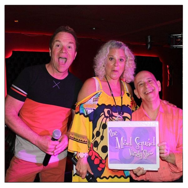 Three people posing with microphones and a sign for The Mod Squad Variety Show.