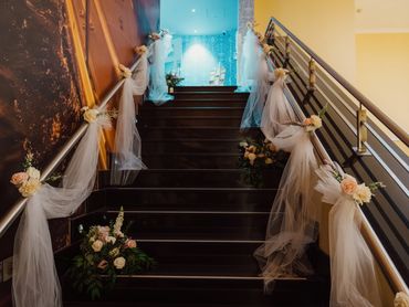 Elegant staircase decorated with white tulle and pastel roses for a wedding.