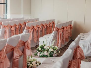 Rows of white chairs with pink bows, floral arrangements, set for a wedding ceremony.
